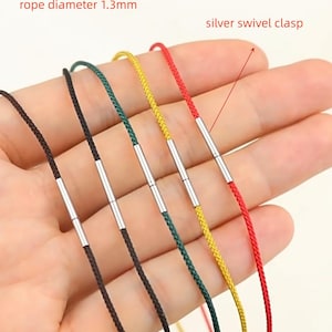 May include: A hand holds several colorful cords with silver swivel clasps. The cords are black, green, yellow, and red. The rope diameter is 1.3mm.