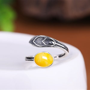 May include: A silver ring with a yellow amber stone and a feather design.
