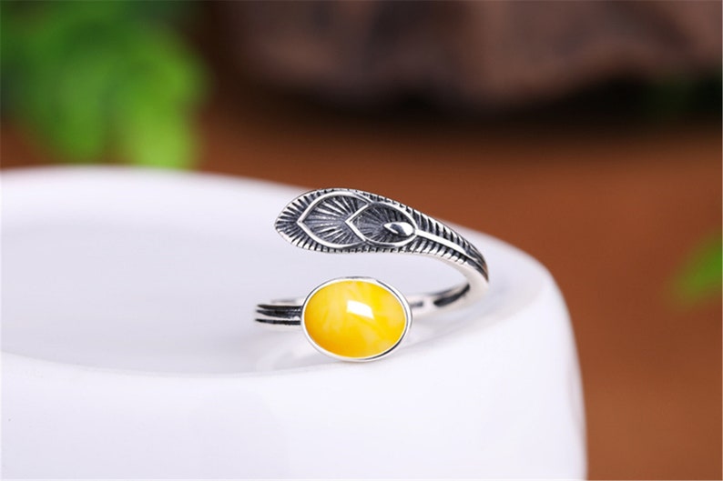 May include: A silver ring with a yellow amber stone and a feather design.