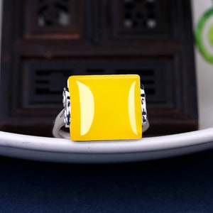May include: A silver ring with a square yellow gemstone. The ring has a decorative design on the band.