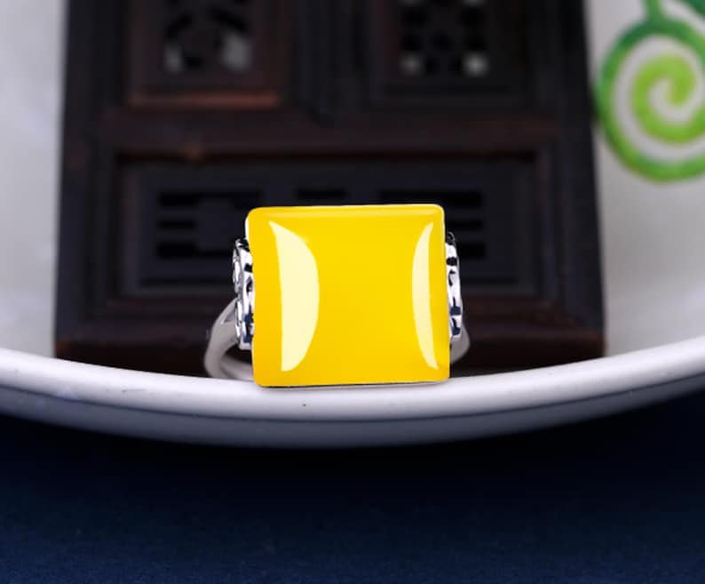 May include: A silver ring with a square yellow gemstone. The ring has a decorative design on the band.