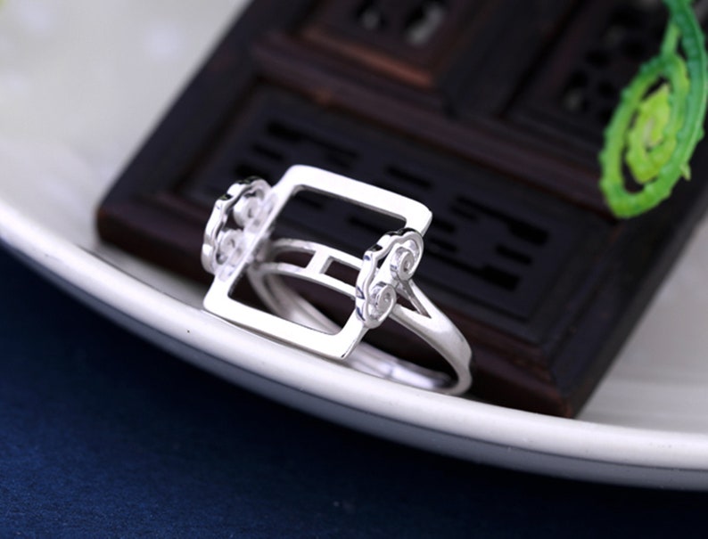May include: A silver ring with a square design and intricate details. The ring is made of sterling silver and has a polished finish.