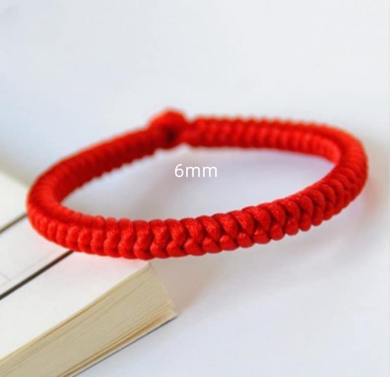 May include: A red braided bracelet with a 6mm width. The bracelet is made of a thick, woven cord.