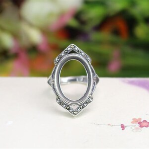 May include: Silver ring with an oval-shaped setting, decorated with small stones around the edge.