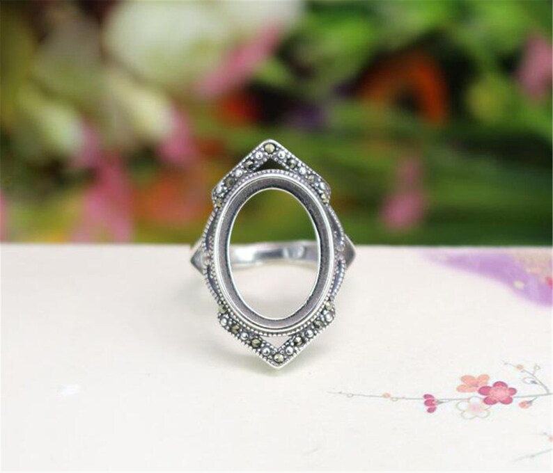 May include: Silver ring with an oval-shaped setting, decorated with small stones around the edge.