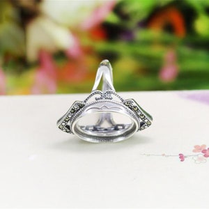 May include: Silver ring with an oval bezel setting and a delicate filigree design. The ring is adorned with small black gemstones.