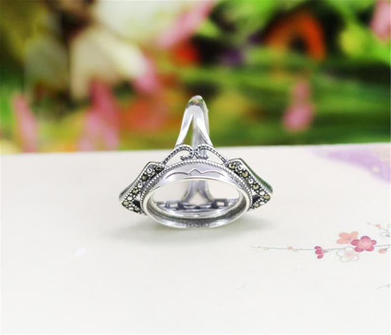 May include: Silver ring with an oval bezel setting and a delicate filigree design. The ring is adorned with small black gemstones.