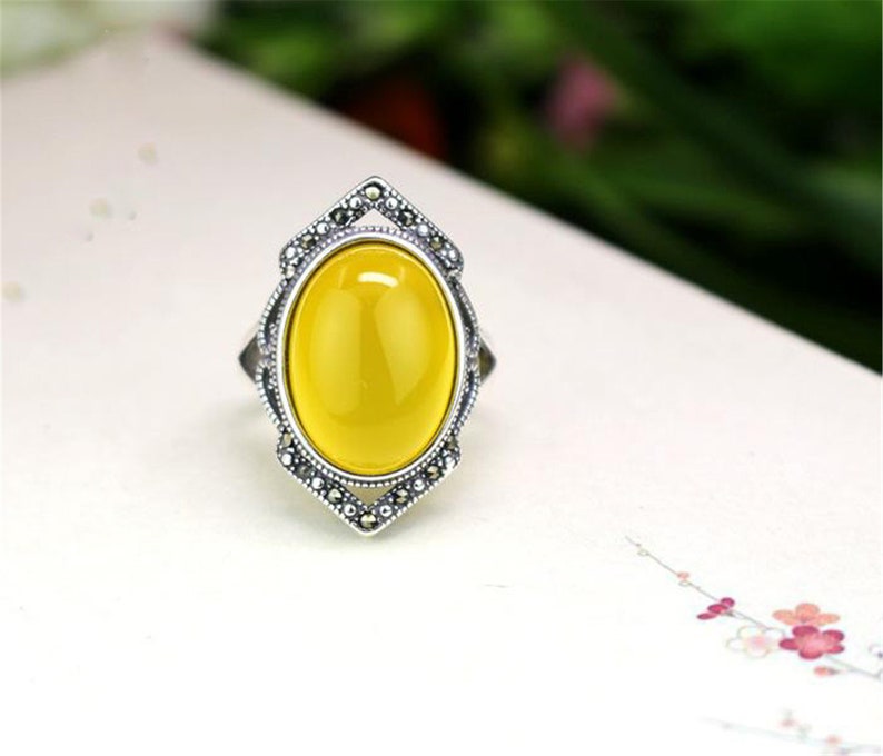 May include: A silver ring with a yellow oval gemstone set in a detailed silver frame. The frame is decorated with small black stones.