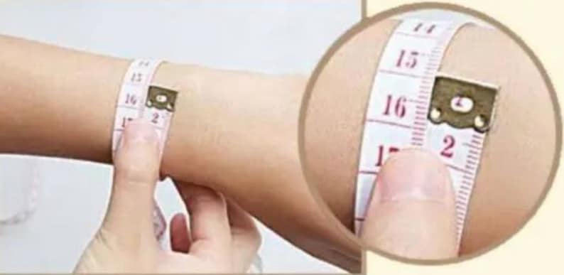 May include: A white measuring tape with red markings is wrapped around a person's wrist. The tape reads 15, 16, and 17 inches.