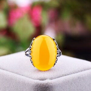 May include: A yellow oval gemstone ring with a silver filigree setting. The ring is on a white velvet box.