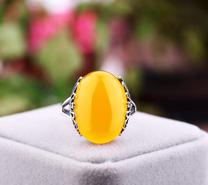 May include: A yellow oval gemstone ring with a silver filigree setting. The ring is on a white velvet box.