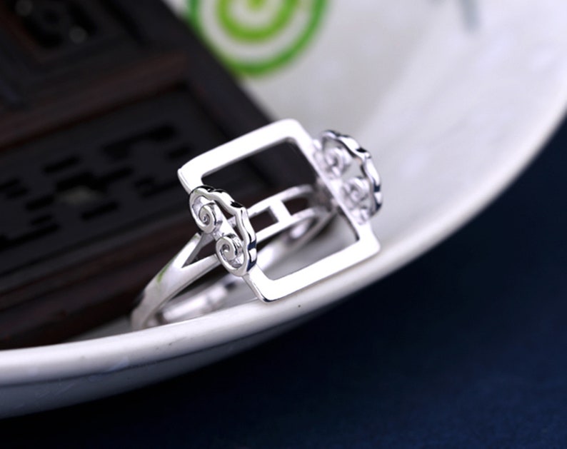 May include: A silver ring with a square design and intricate cloud-like details. The ring is made of sterling silver and has a polished finish.
