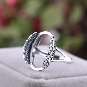 May include: Silver ring with an oval-shaped setting and intricate floral details. The ring is designed to hold a gemstone or other embellishment.
