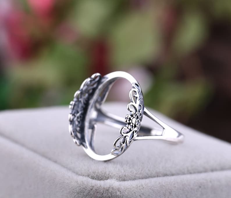 May include: Silver ring with an oval-shaped setting and intricate floral details. The ring is designed to hold a gemstone or other embellishment.