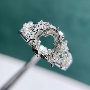 May include: Silver ring setting with a star-shaped design and a large oval-shaped center stone setting. The ring is set with small diamonds around the center stone setting.
