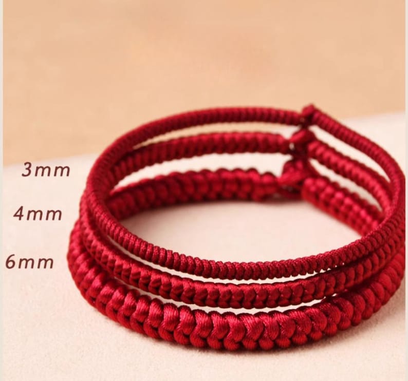 May include: Three red braided cords, each with a different thickness: 3mm, 4mm, and 6mm. The cords are knotted together to create a bracelet.