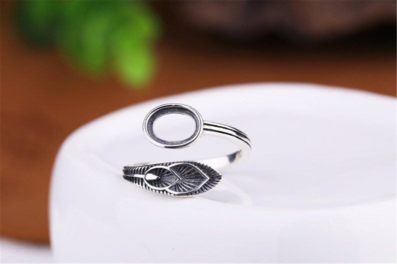 May include: Silver ring with an oval-shaped bezel and a leaf design. The ring is adjustable and can be worn on any finger.