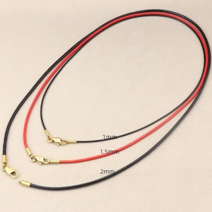 Può includere: Tre cordini per collana neri e rossi, con chiusure color oro. I cordini hanno un diametro di 1 mm, 1,5 mm e 2 mm. L'immagine mostra i cordini su uno sfondo neutro, con le misure indicate.