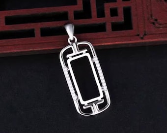 Puede incluir: Un colgante plateado con un centro rectangular negro y un marco decorativo. El marco está adornado con pequeñas piedras transparentes a los lados. El colgante cuelga de un lazo plateado.