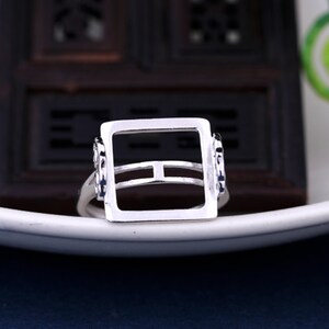 May include: A silver ring with a square-shaped setting. The setting has a double band design and is open on all sides.