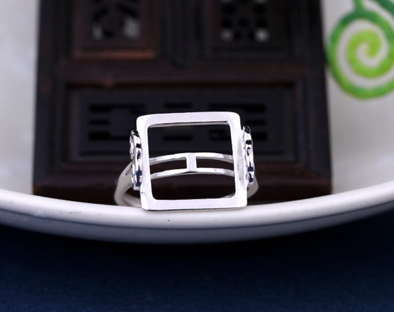 May include: A silver ring with a square-shaped setting. The setting has a double band design and is open on all sides.