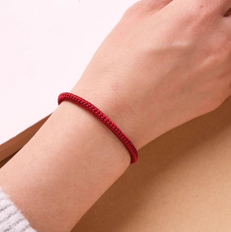 May include: A red braided string bracelet on a person's wrist.