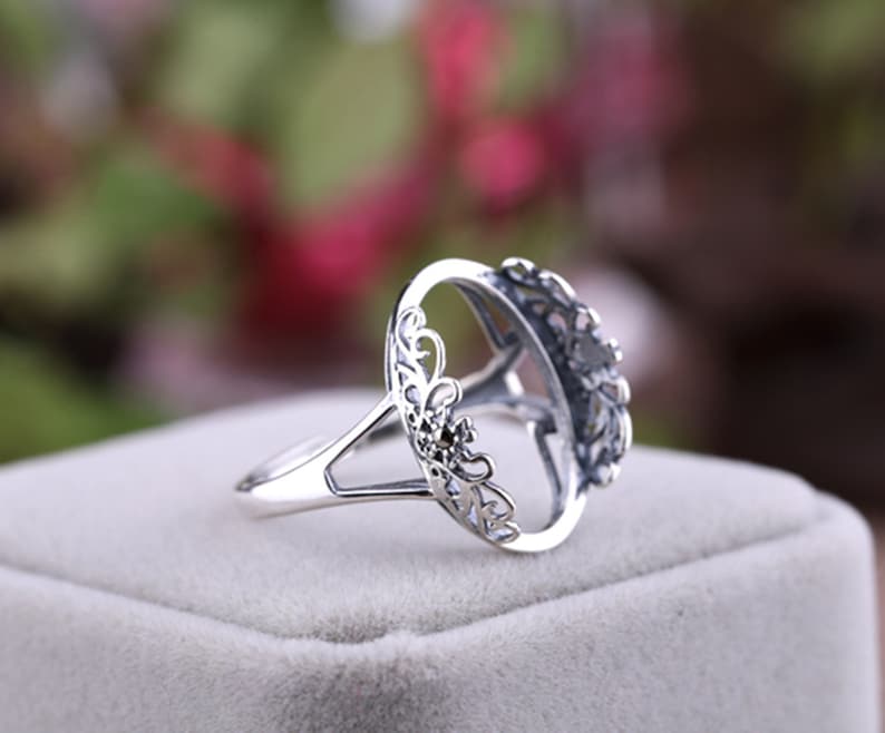 May include: Silver ring with an oval-shaped setting, featuring a delicate, intricate floral design. The setting is open, allowing for a stone to be inserted.