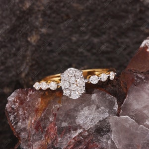 May include: A gold band ring with a large cluster of round diamonds in the center and smaller diamonds set along the band.