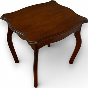 May include: A small, antique wooden side table with a dark brown finish. The table has a unique, curved top and four curved legs. The table measures approximately 61 cm long, 61 cm wide, and 51 cm high.