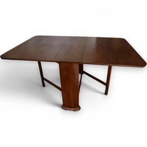 May include: A dark brown, rectangular drop-leaf table with a central support and angled legs. The table is made of wood and has a glossy finish. The table is approximately 122 cm long when fully extended.