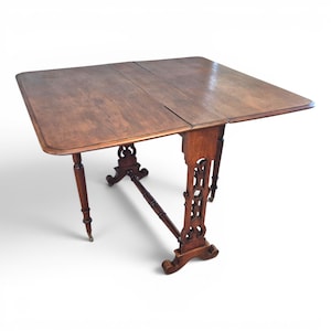 May include: An antique drop-leaf table in dark brown wood. The table has a square top with carved supports and legs, and brass feet. The leaves are extended, creating a larger surface. The table's dimensions are approximately 90 cm x 90 cm.
