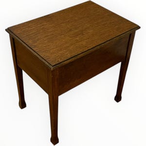 May include: A small, rectangular wooden table with a dark brown finish. The table has four slender legs and a simple, classic design. The tabletop and sides show the wood grain. The table is likely a side table or small accent piece.