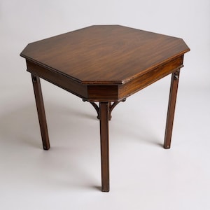 May include: A dark brown, octagonal wooden table with four slender legs. The table has a decorative edge and a smooth, polished surface. The legs are slightly angled, and the table appears to be antique.