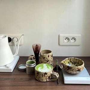 Handmade Nordic Pottery matcha set, styled in a kitchen setting with whisk holder and matcha tools. There's a beautiful matcha latte in the mug.