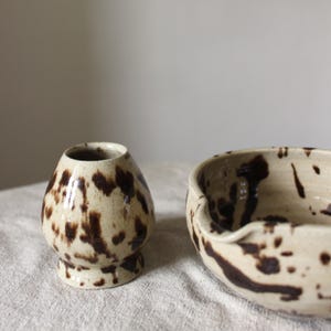 A ceramic matcha bowl and a whisk holder, both in a speckled brown glaze.