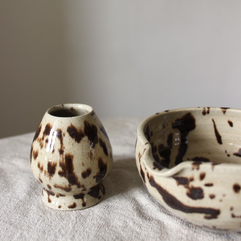 A ceramic matcha bowl and a whisk holder, both in a speckled brown glaze.