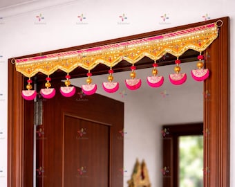 May include: A decorative door valance in gold and pink, featuring detailed beadwork and hanging pink tassels. The valance is mounted above a wooden door frame, enhancing the entrance with a touch of elegance and colour.