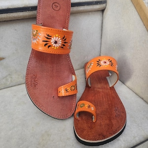 Op de afbeelding: Een paar oranje leren sandalen met bloemmotieven. De sandalen hebben een teensluiting en een band over de bovenkant van de voet. De binnenzool is bruin en de zool is zwart. Maat 40 (ongeveer 25 cm).
