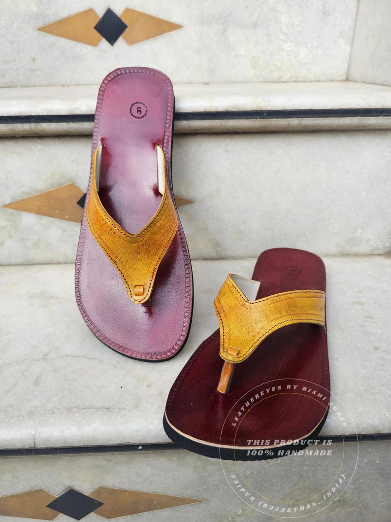 Pode incluir: Um par de sand&aacute;lias de couro feitas &agrave; m&atilde;o. As sand&aacute;lias t&ecirc;m uma base bord&ocirc; escura com uma tira amarela. A sola &eacute; preta. As sand&aacute;lias s&atilde;o tamanho 6. O texto "LEATHEREYES BY RISHI SHOES" e "THIS PRODUCT IS 100% HANDMADE" s&atilde;o vis&iacute;veis.