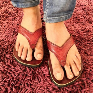 May include: A pair of red leather flip-flops with a black sole. The flip-flops are on a red shag carpet.