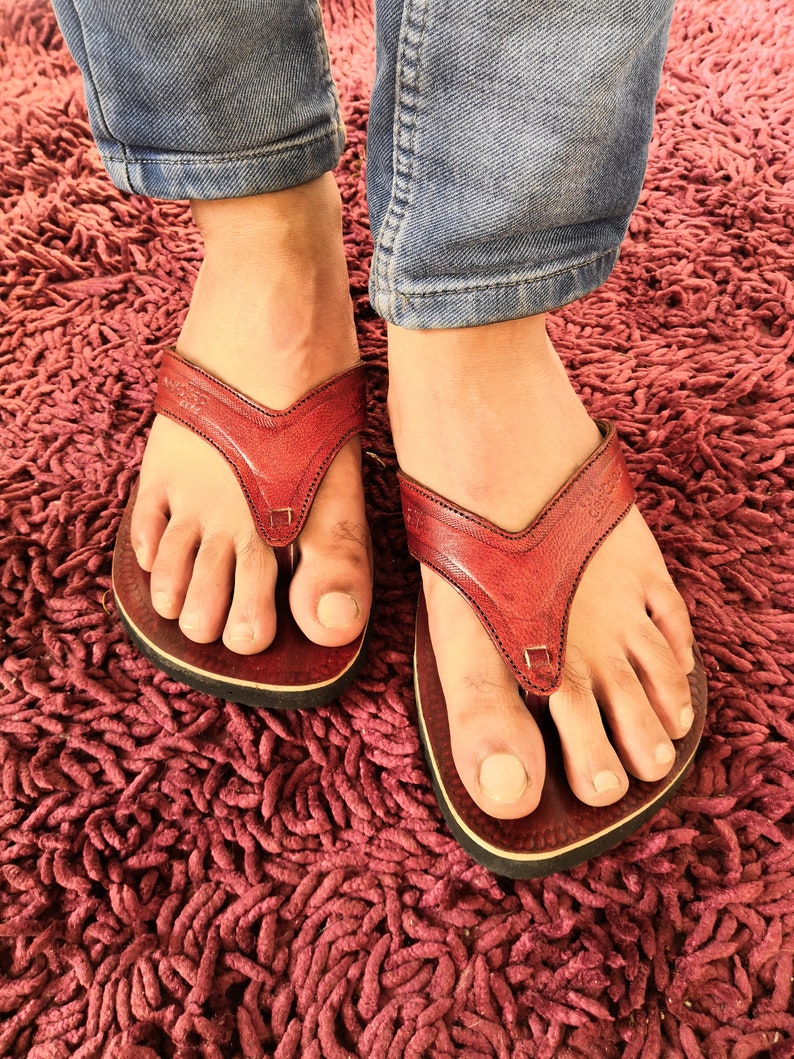 May include: A pair of red leather flip-flops with a black sole. The flip-flops are on a red shag carpet.
