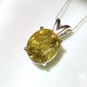 May include: A pendant featuring an oval-shaped, faceted yellow gemstone set in a silver-toned metal prong setting. The gemstone displays a textured, crackled appearance throughout its surface. The pendant is attached to a thin, light-colored chain.