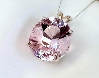 May include: A light pink oval gemstone pendant with a silver setting. The gemstone is faceted, reflecting light. The pendant hangs from a thin silver chain, showcasing a piece of jewelry.