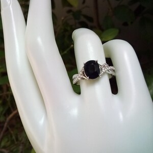 Puede incluir: Anillo plateado con una gran piedra negra ovalada. El anillo presenta piedras preciosas m&aacute;s peque&ntilde;as y transparentes a lo largo de la banda, creando un efecto brillante. El dise&ntilde;o es elegante y cl&aacute;sico.