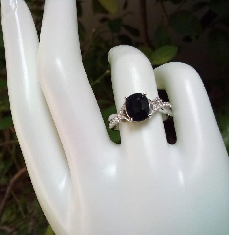 Puede incluir: Anillo plateado con una gran piedra negra ovalada. El anillo presenta piedras preciosas m&aacute;s peque&ntilde;as y transparentes a lo largo de la banda, creando un efecto brillante. El dise&ntilde;o es elegante y cl&aacute;sico.