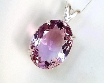 May include: An oval-cut, faceted purple gemstone pendant set in a silver-toned metal prong setting. The stone displays a gradient of light to deep violet hues. The pendant is attached to a thin, delicate silver-colored chain at the top bail.