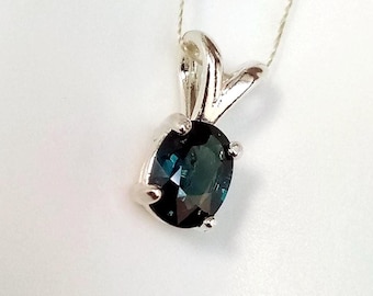 May include: A silver pendant necklace featuring an oval, dark teal gemstone. The gemstone is set in a silver bezel with a decorative bail. The necklace is displayed on a white background.