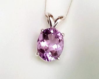 May include: A silver pendant necklace featuring a large, oval-cut amethyst gemstone. The gemstone is a light purple color and is set in a silver bezel with a simple bail. The necklace is displayed against a white background.