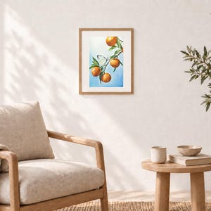 K&ouml;nnte beinhalten: Ein gerahmter Wandkunstdruck mit einer Aquarellillustration eines Zweigs mit vier leuchtend orangefarbenen Zitrusfr&uuml;chten und gr&uuml;nen Bl&auml;ttern vor einem sanft blauen Hintergrund, mit einem kleinen wei&szlig;en Schmetterling auf dem Zweig.