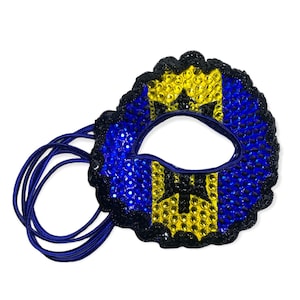Könnte beinhalten: Eine blaue, gelbe und schwarze Maskenballmaske mit Strasssteinen. Die Maske ist an einem blauen Gummiband befestigt.